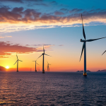 **A vast offshore wind farm at sunset in the Aegean Sea, Turkey. Modern wind turbines are silhouetted against a colorful sky, with the coastline visible in the distance. Calm seas reflect the turbine lights, showcasing sustainable energy generation in a picturesque setting.**